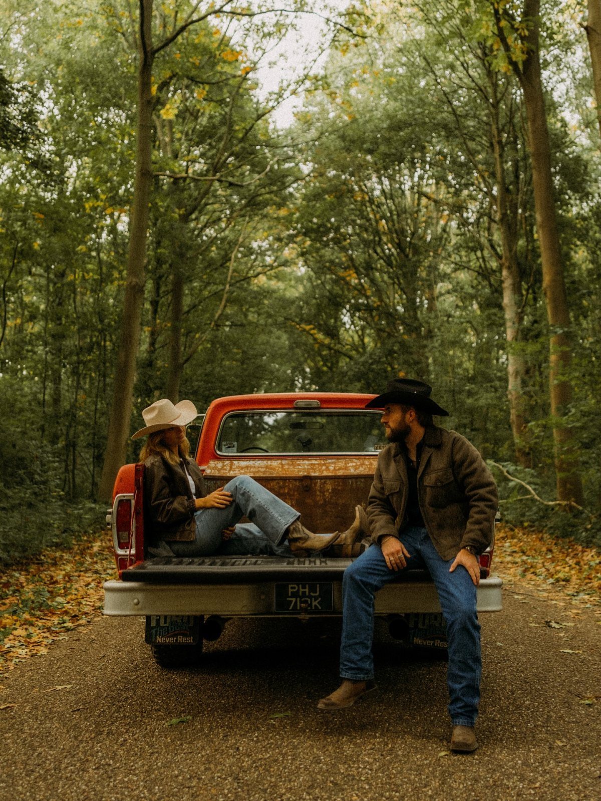 Couple in western wear posing with a red vintage truck in a forest