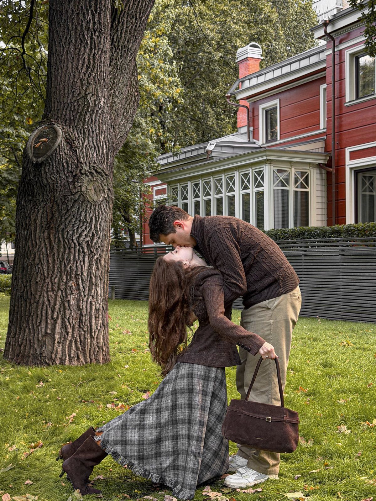 Couple kissing in a garden wearing brown sweaters and a plaid skirt.