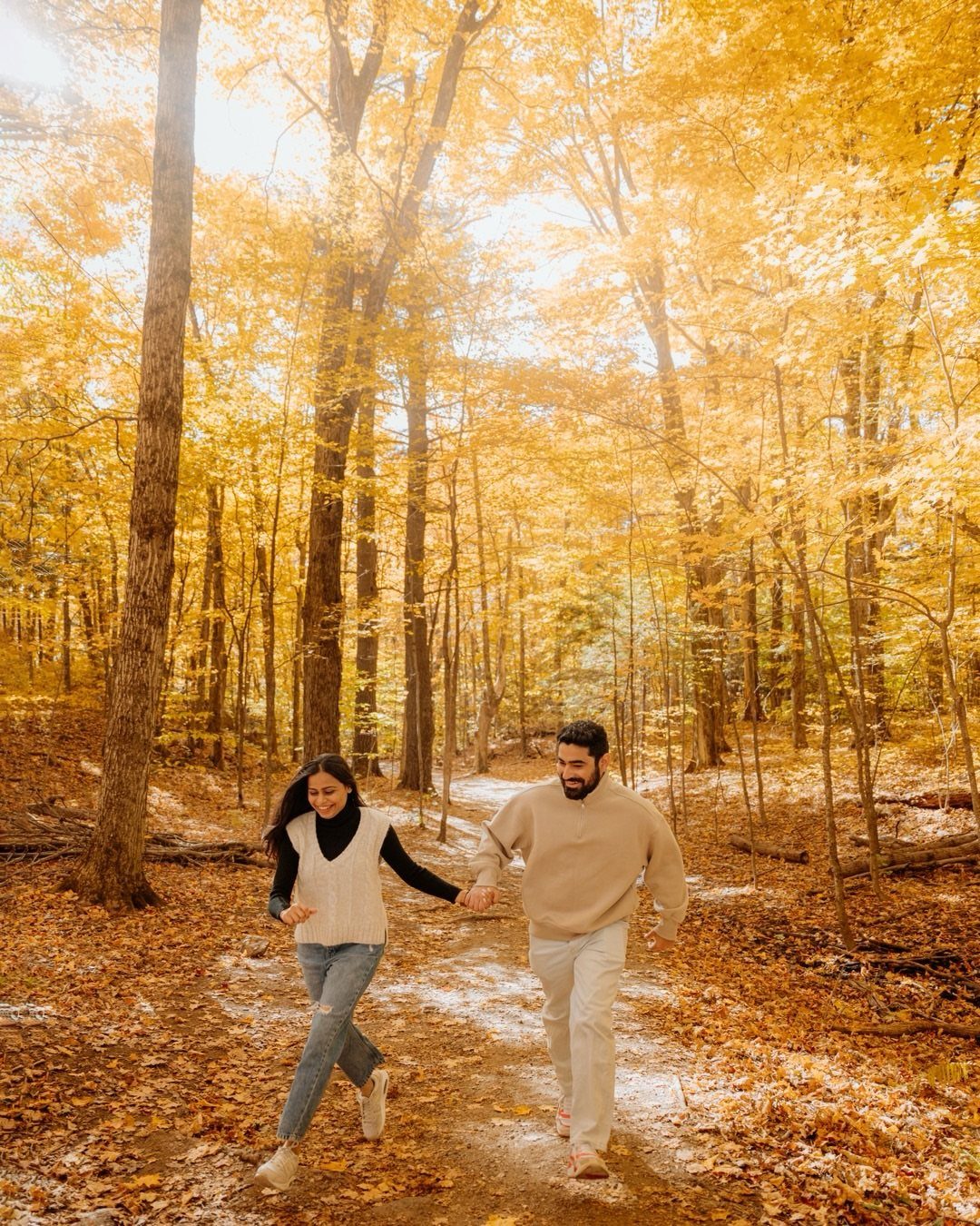 Couple walking hand-in-hand through a forest with vibrant yellow autumn foliage.