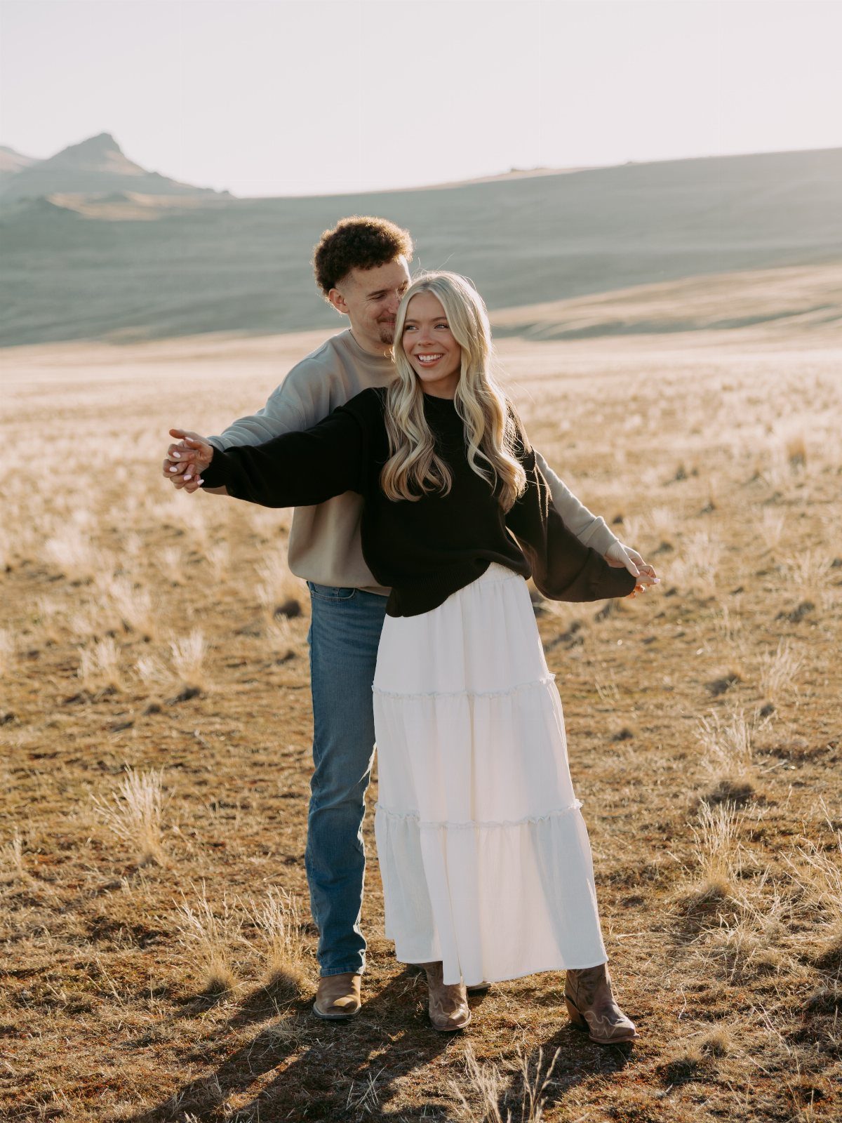 Smiling couple in a field wearing a black knit sweater and white tiered skirt.