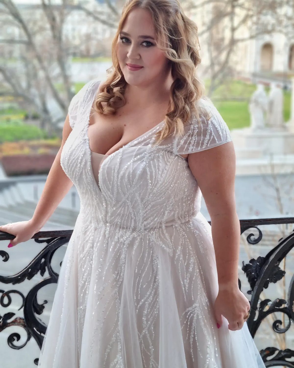 Plus-size bride in a sequined white wedding gown posing on a balcony