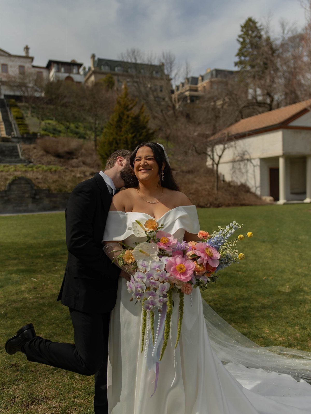 Plus size bride in white gown holding colorful bouquet with groom hugging her