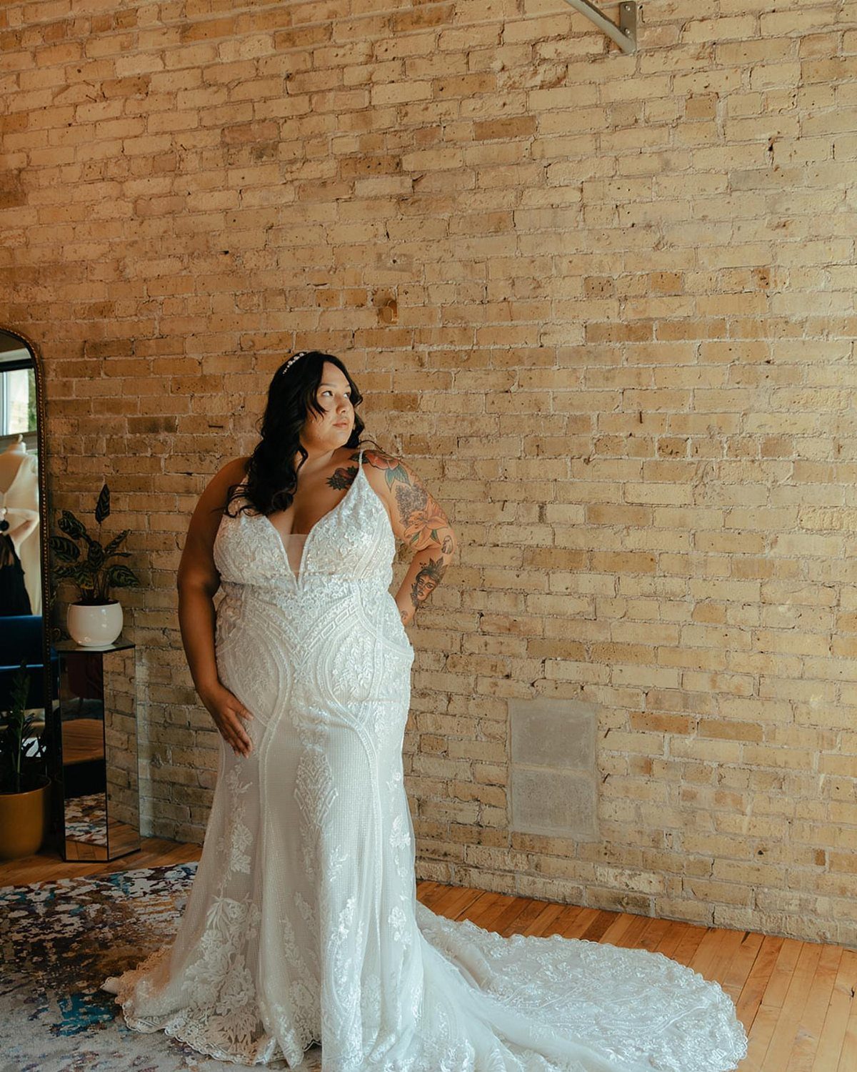 Plus-size bride in a white lace fit-and-flare wedding dress against a brick wall.