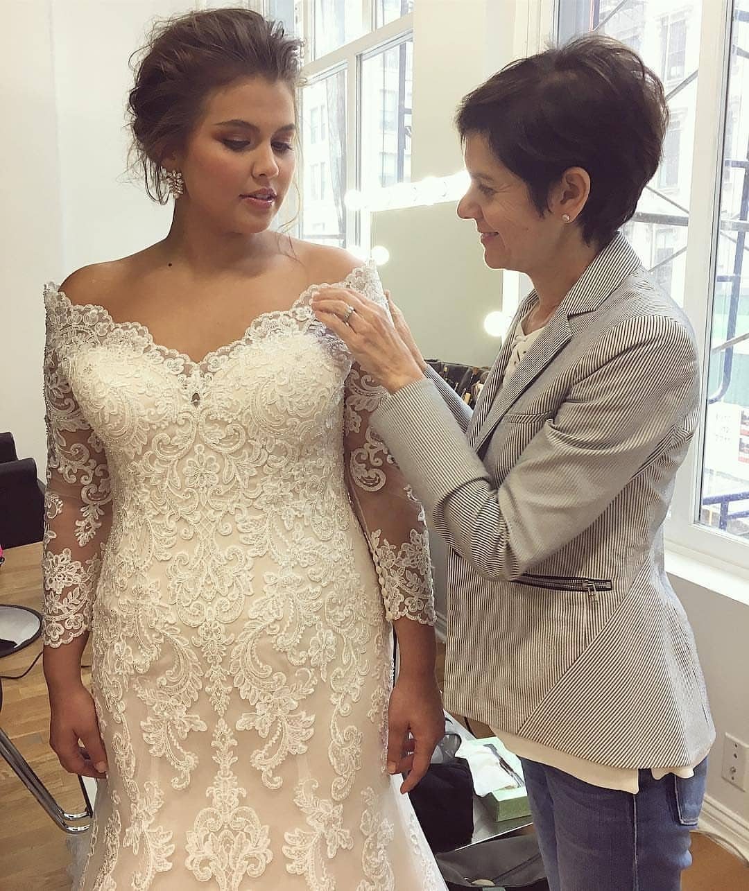Plus size bride in a white lace wedding dress being fitted by a stylist