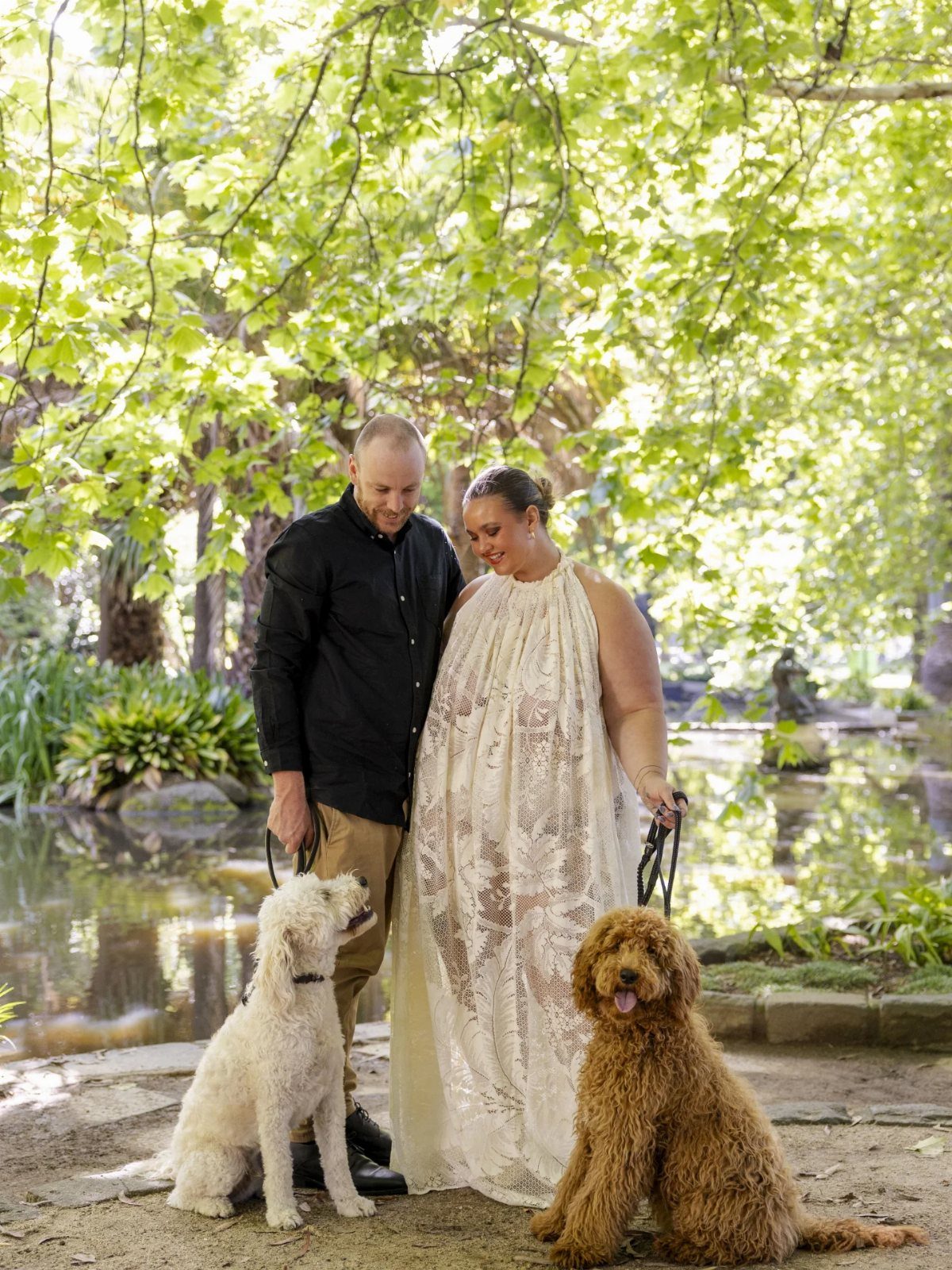 Plus size bride and groom standing with two dogs by a garden pond