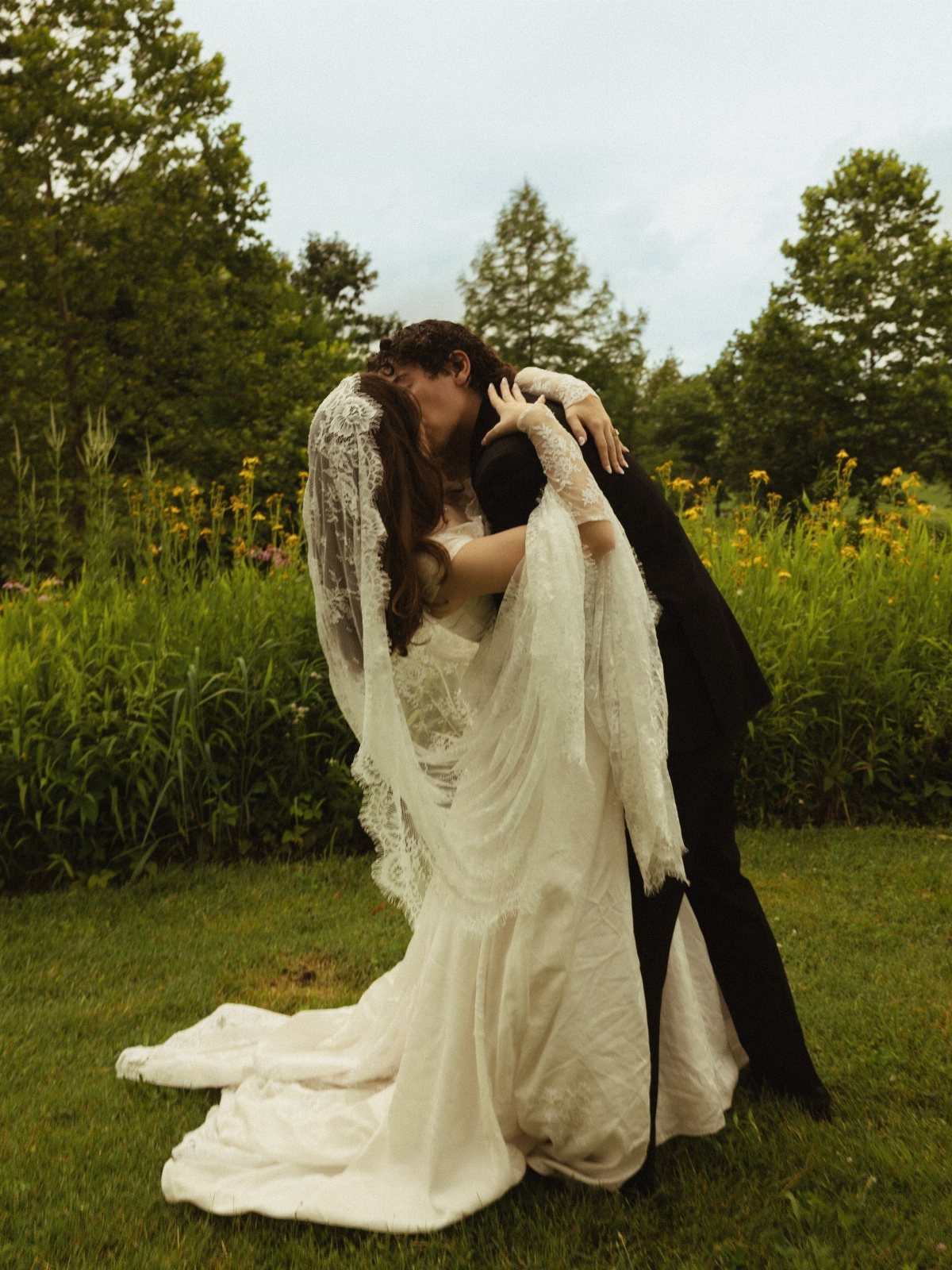Plus-size bride in lace gown kissing groom in a lush green field