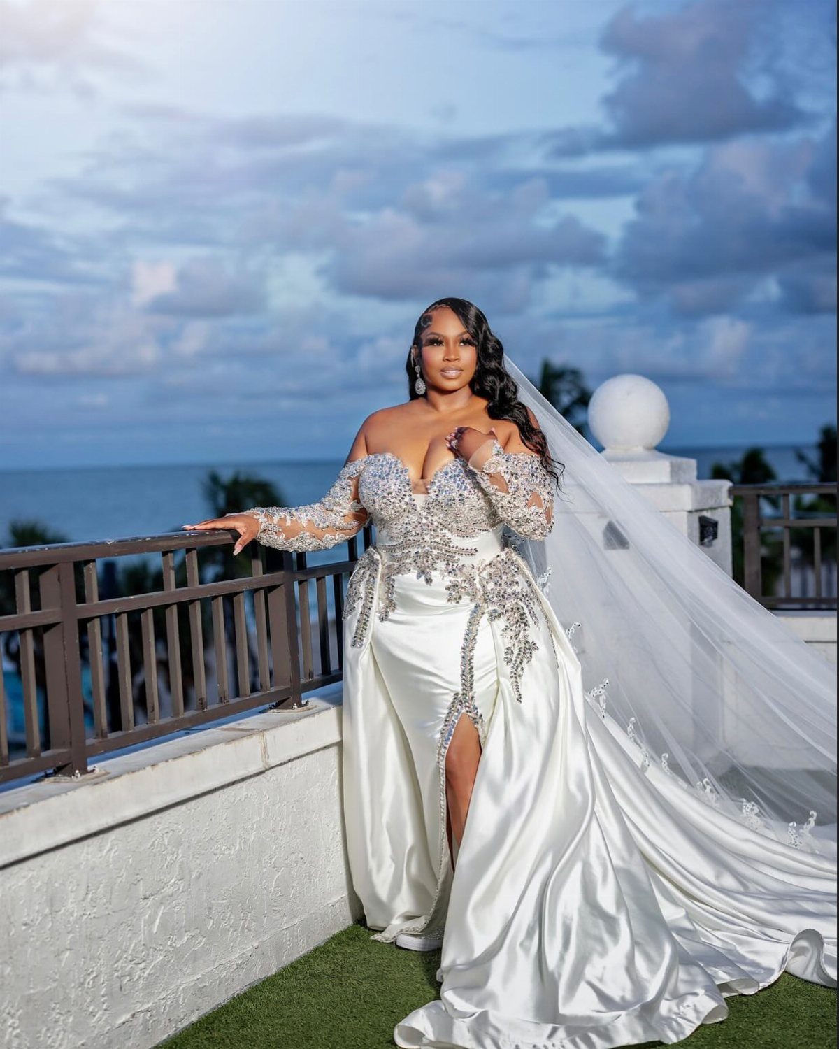 Plus-size bride in an embellished white gown posing on a balcony by the ocean