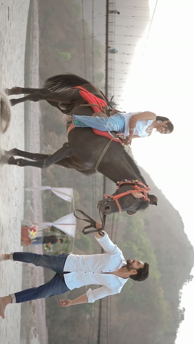 Couple posing with a dark horse against a backdrop of mountains and river.