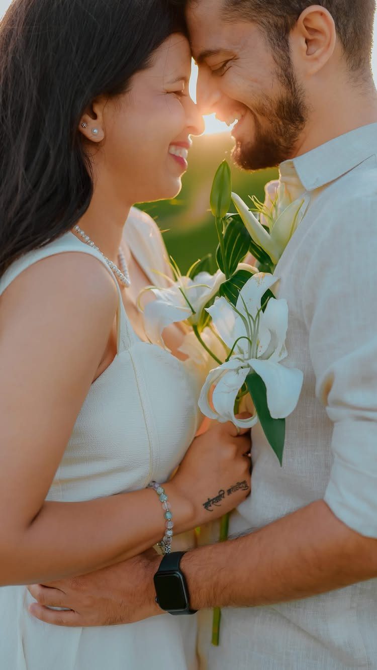Smiling couple in white outfits embracing with white lilies during golden hour sunset