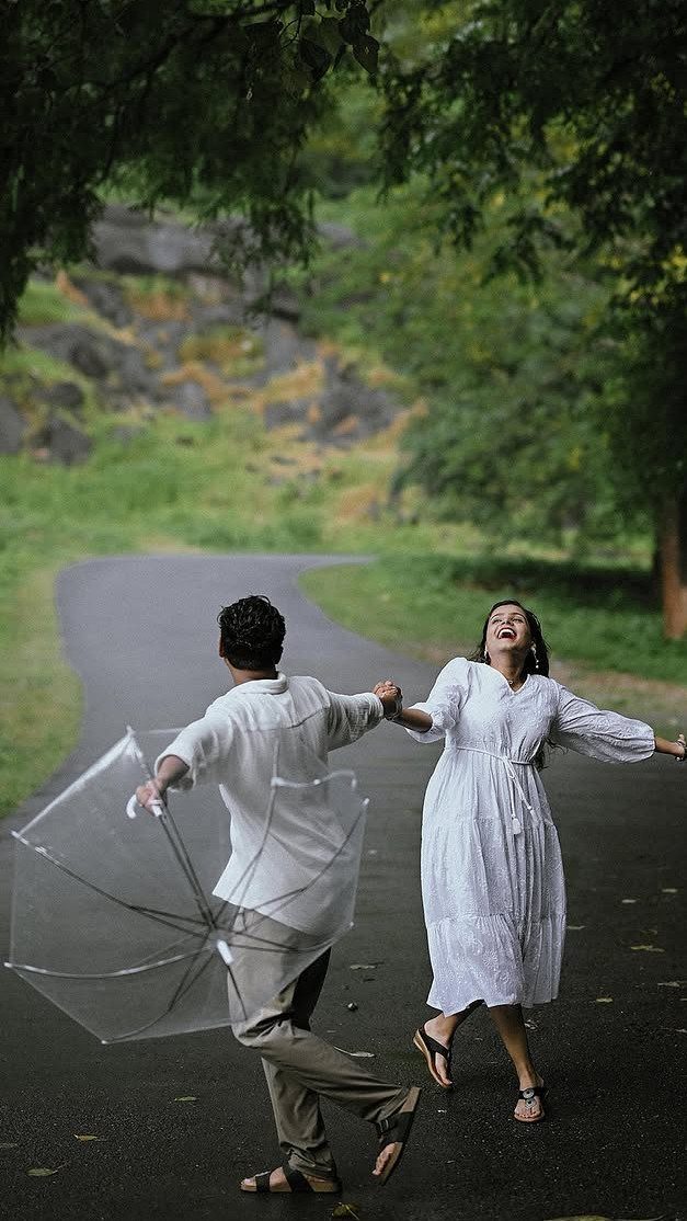 Couple in white clothing laughing and walking on a rainy road with umbrella