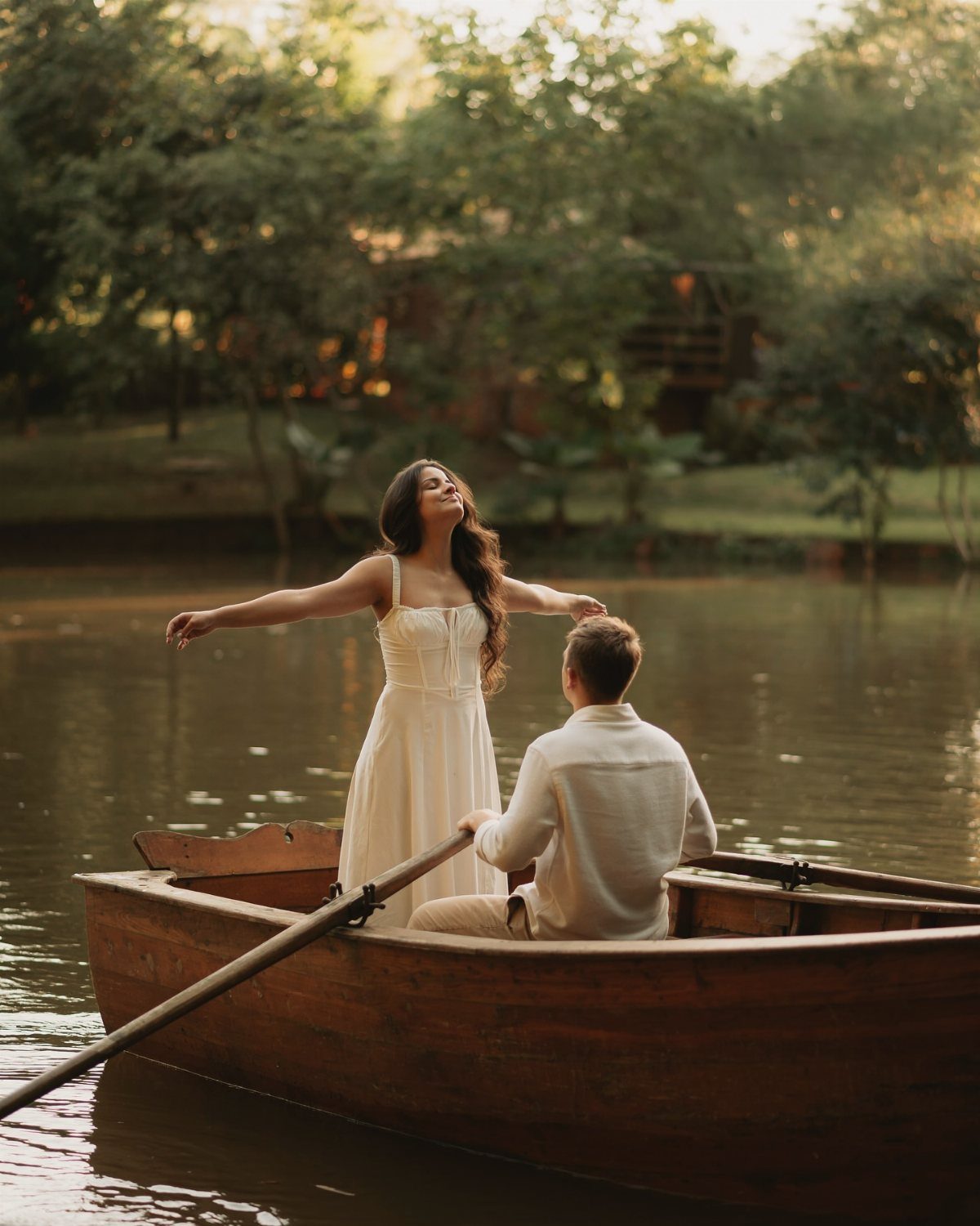 Couple in a wooden rowboat on a lake surrounded by green trees