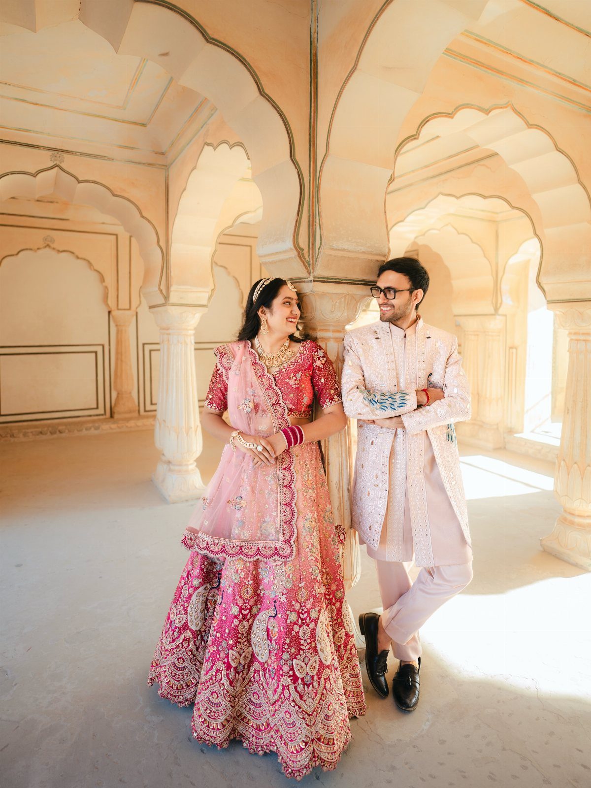 Couple in vibrant pink traditional Indian attire posing inside a carved stone palace.