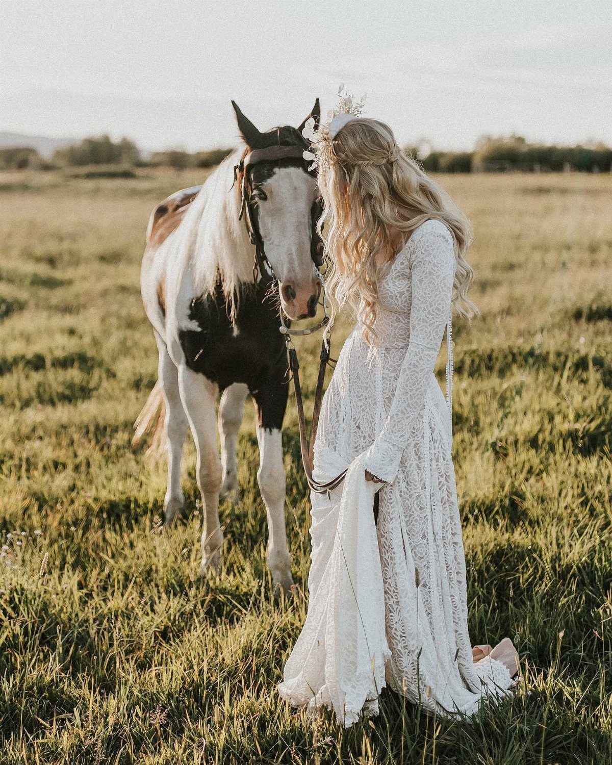 Woman in a white lace bohemian dress standing with a horse in a field