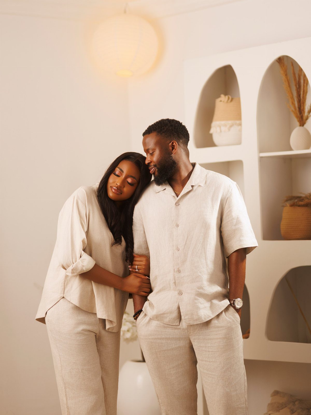Couple wearing matching beige linen outfits posing in a bright, minimalist room.