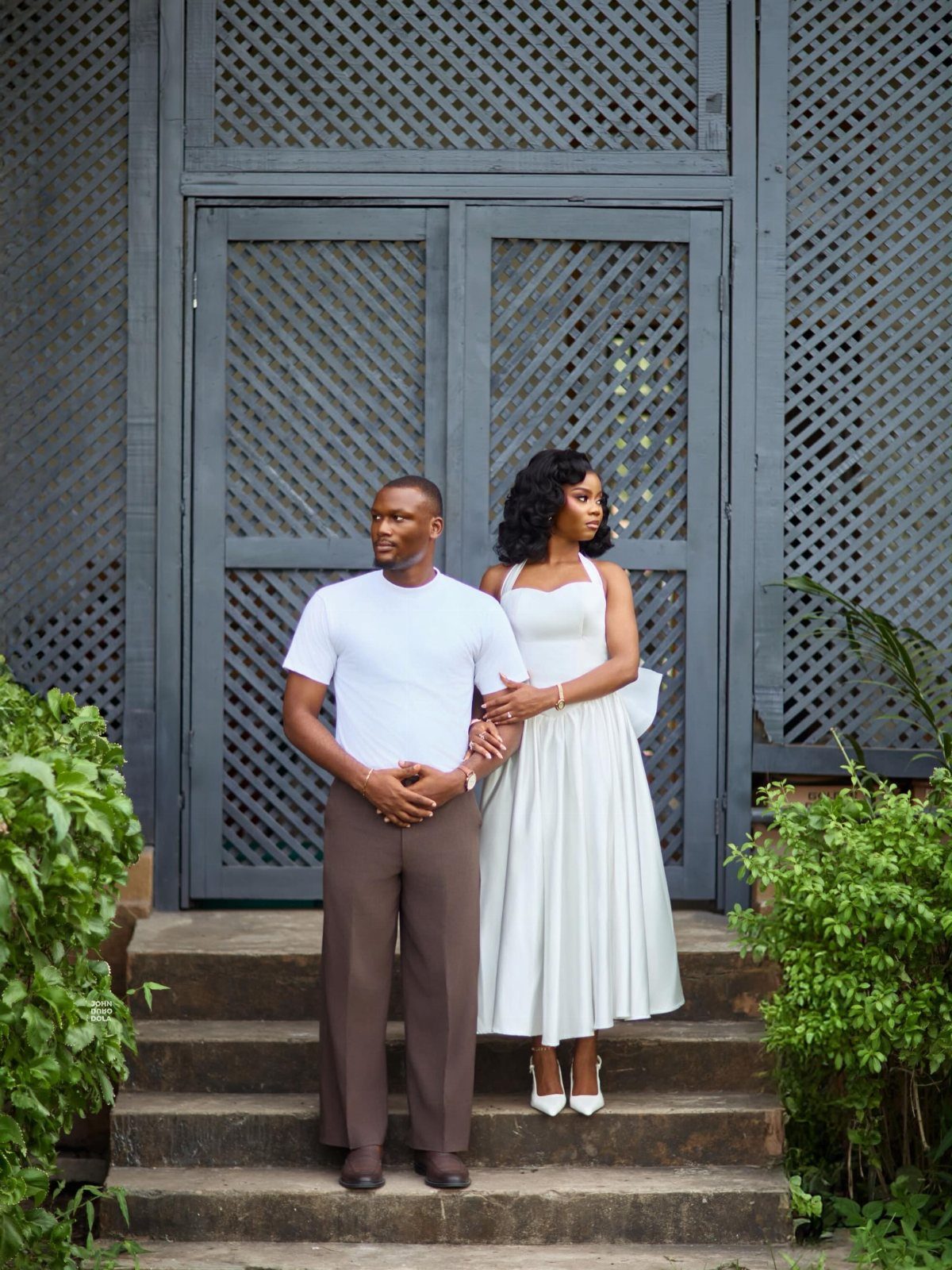 Couple posing on steps, woman wearing an elegant white sleeveless midi dress.