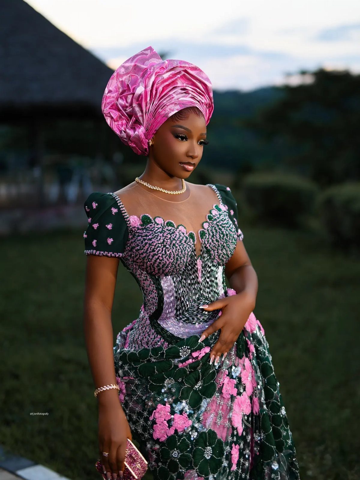 Woman in traditional African attire with a pink headwrap and green lace gown.