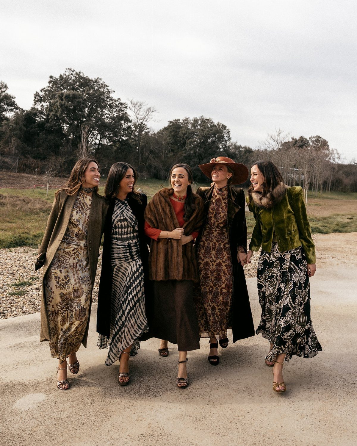 Five women walking outdoors wearing layered autumn outfits with long coats and dresses.