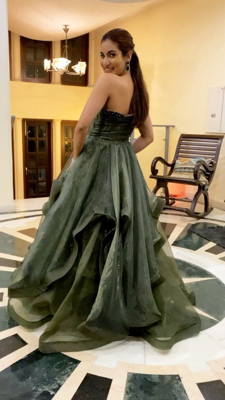 Woman in a voluminous olive green strapless gown posing on a marble floor.