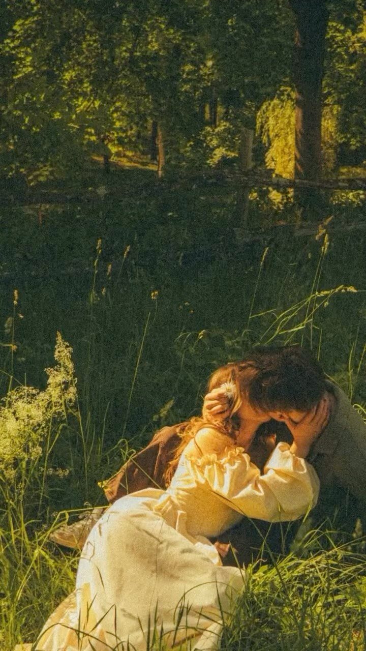 Couple embracing in a grassy field, woman wearing a cream vintage-style dress.