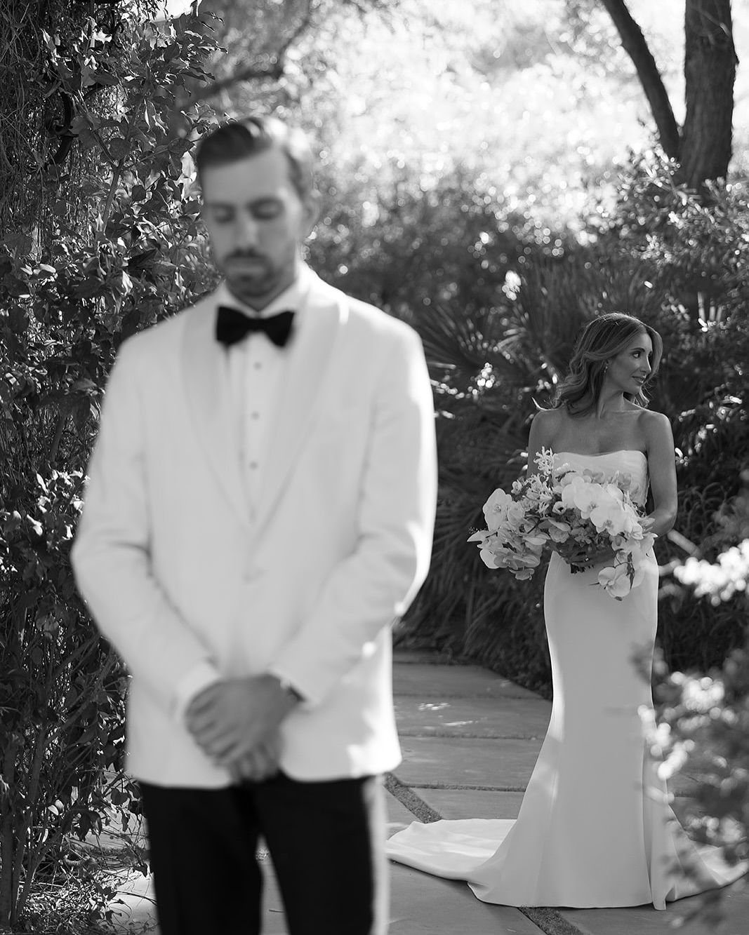 Groom in white tuxedo and bride in white gown in black and white photography