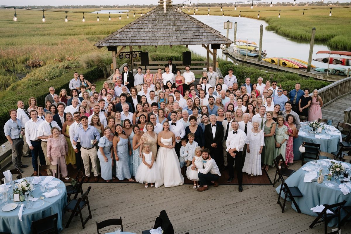 Large group of wedding guests posing for a portrait on a wooden deck.