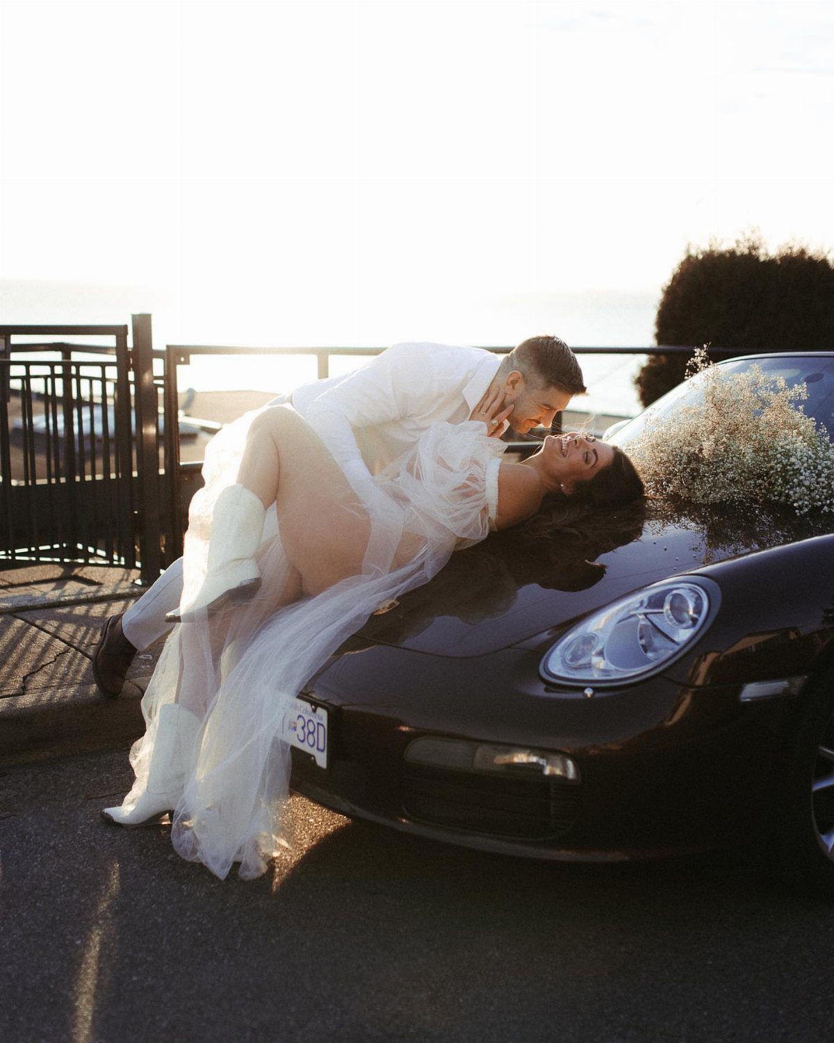 Couple posing romantically with the woman lying on a dark car hood.