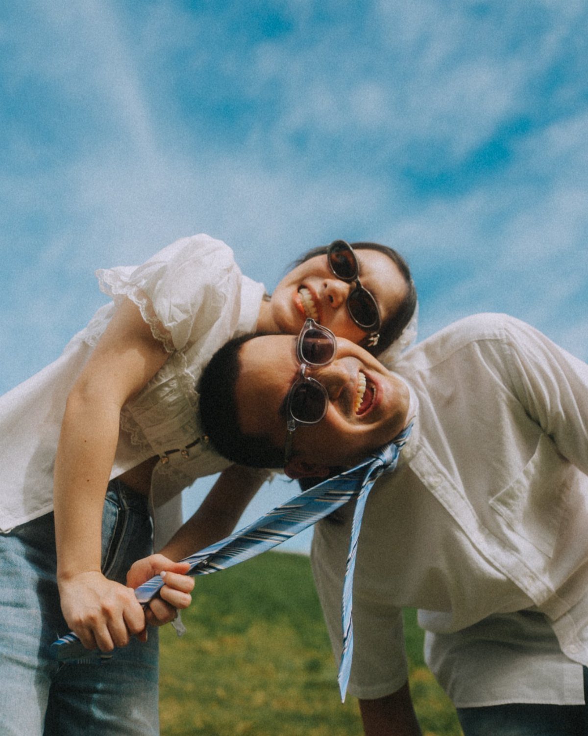 Playful couple laughing while woman pulls man's tie in a grassy field