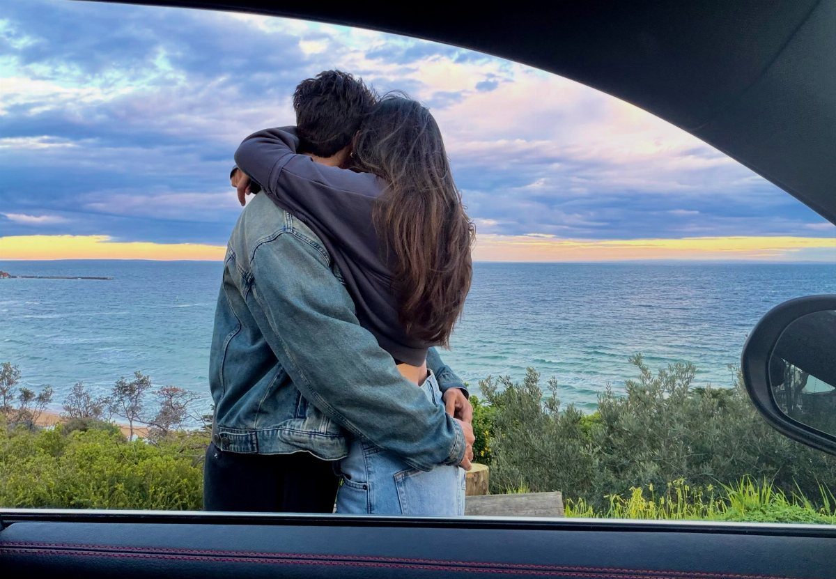 Couple embracing from behind while looking at a scenic ocean view from a car