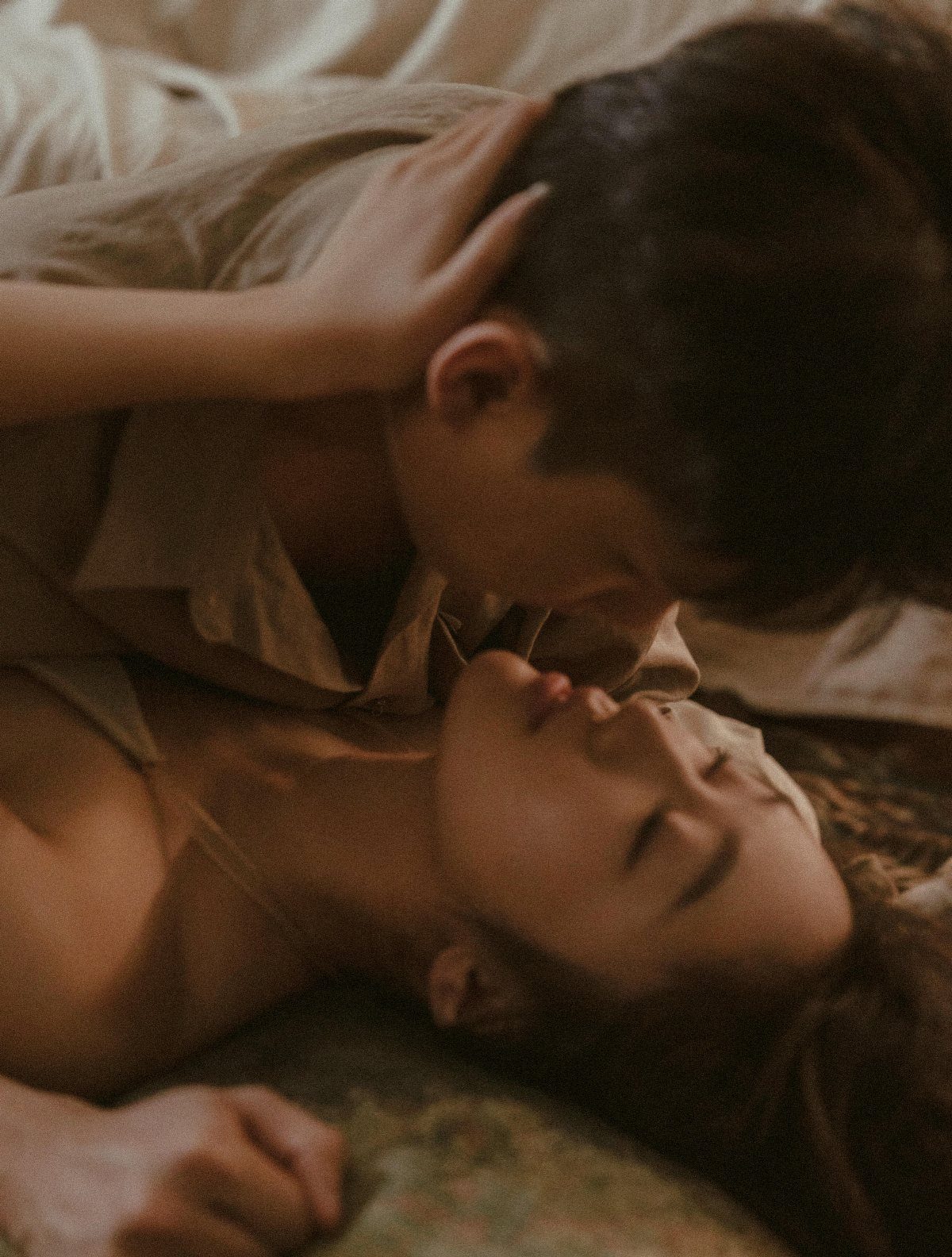 Couple lying together on a bed in an intimate, close-up embrace.