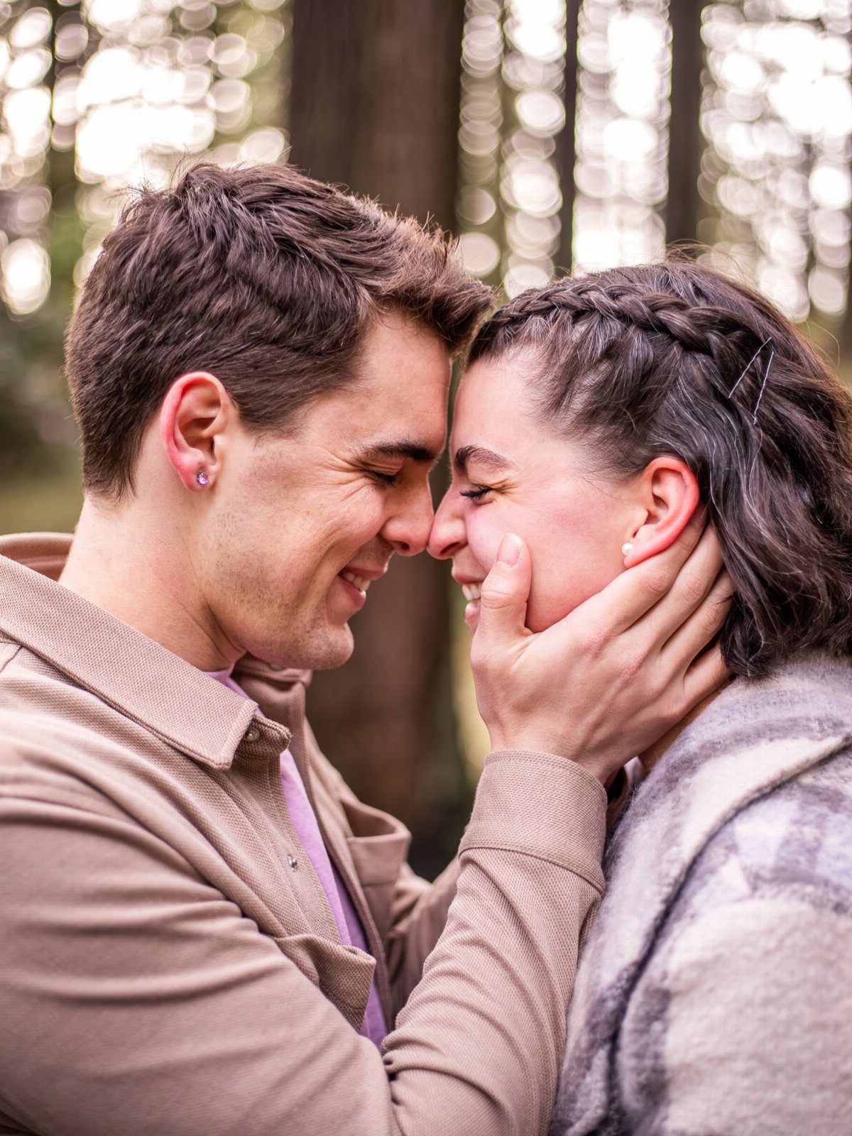 Couple smiling with noses touching in a forest, man holding woman's face.