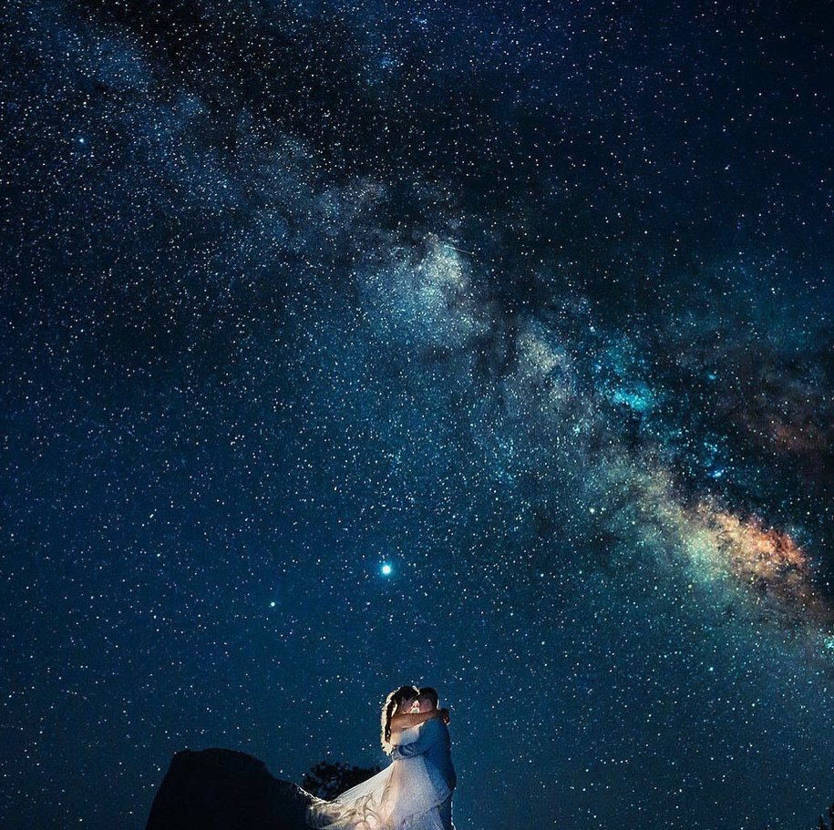 Couple embracing under a brilliant starry night sky with the Milky Way galaxy.