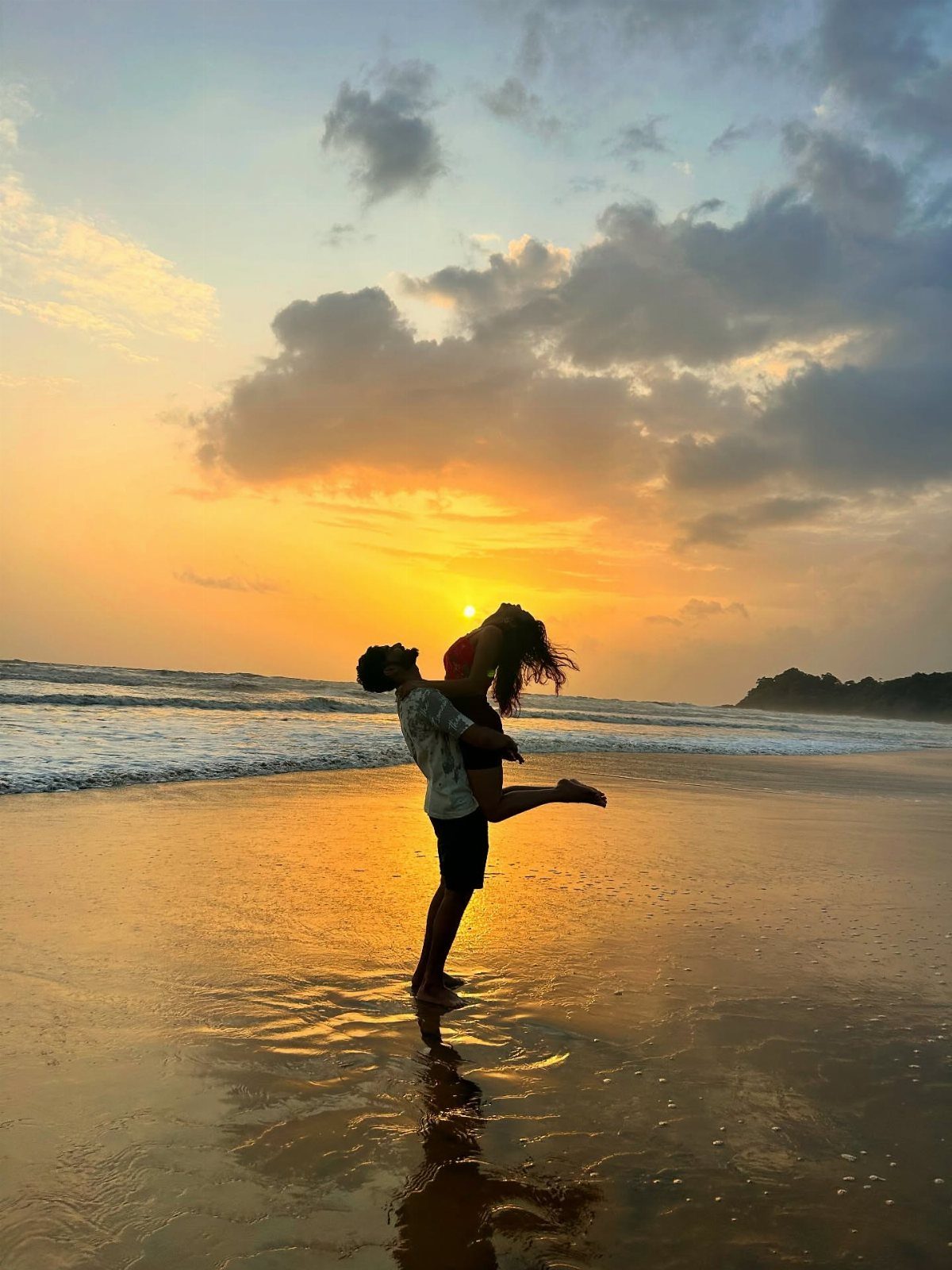 Silhouetted couple embracing on a beach during a vibrant orange sunset over the ocean.
