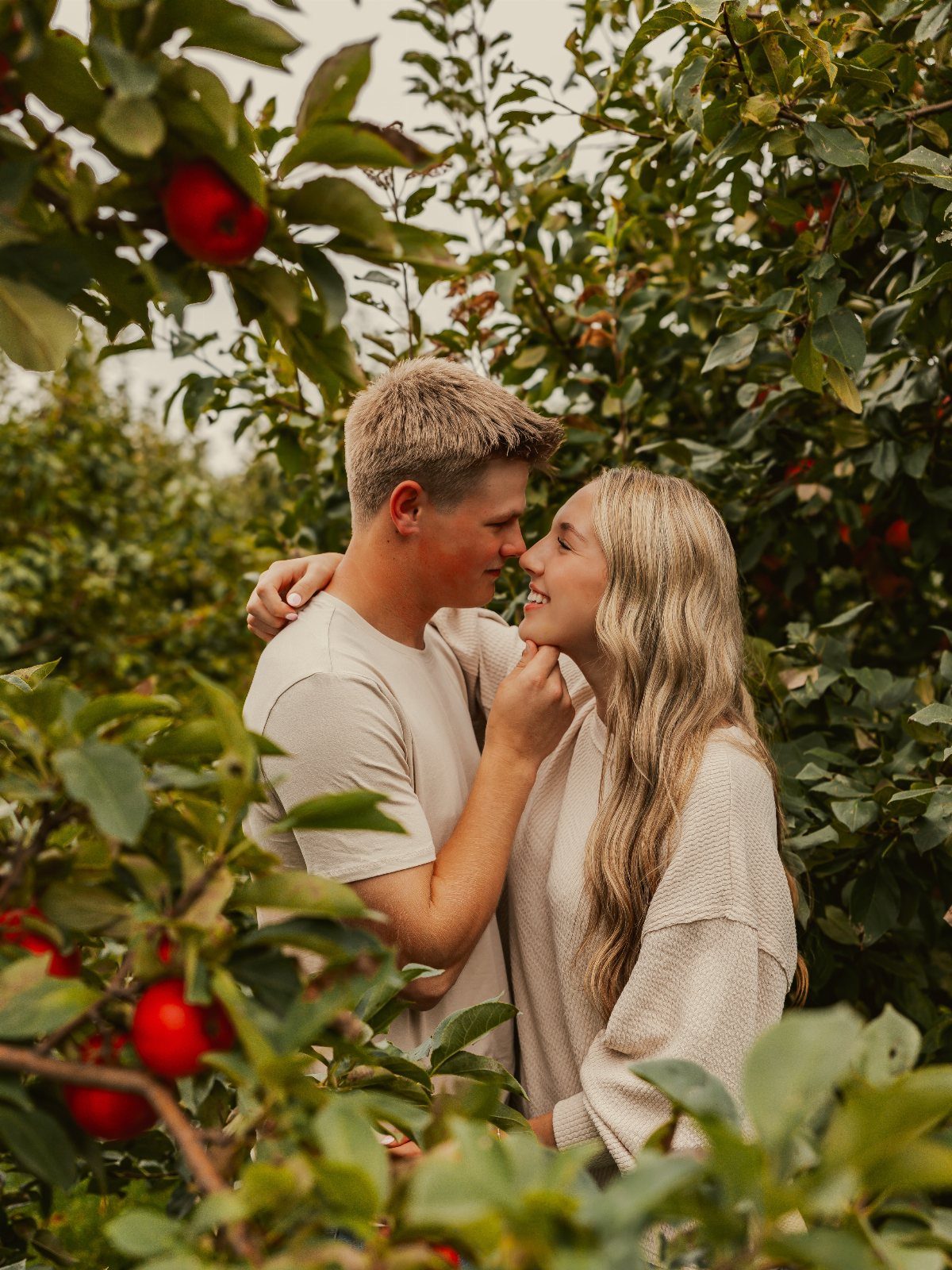 Young couple gazing at each other while standing among red apple trees.