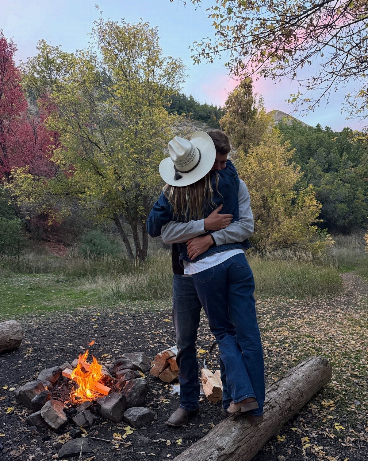 Couple embracing and kissing next to a glowing bonfire in an autumn forest.