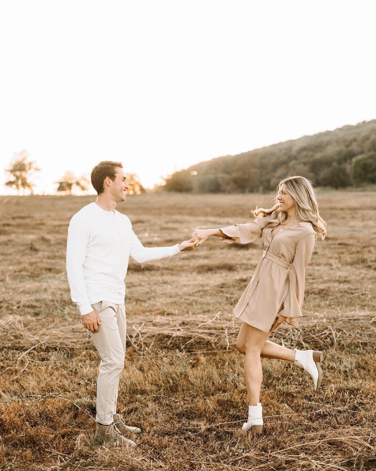 Couple holding hands and dancing in a golden autumn field at sunset.