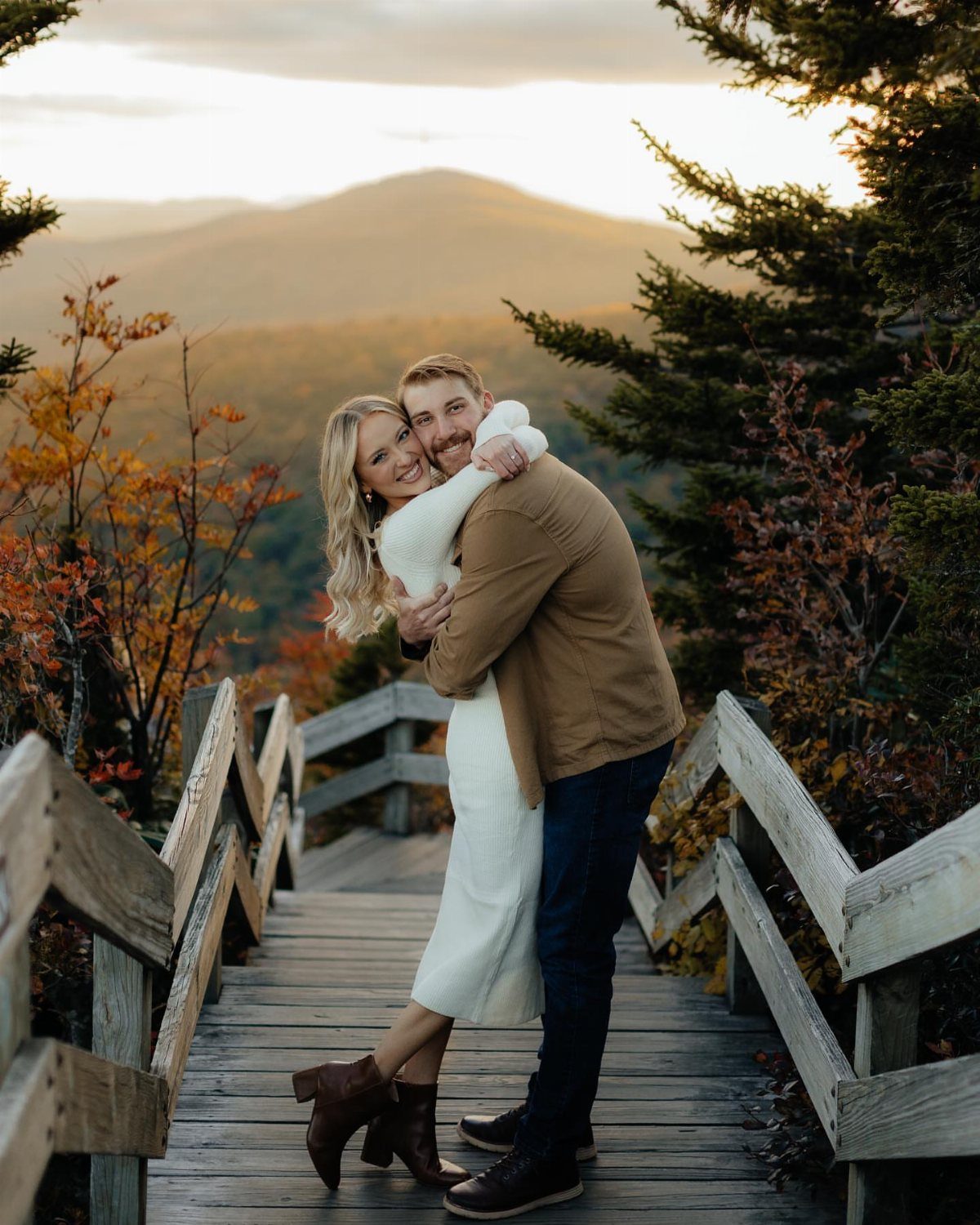Smiling couple embracing on a wooden boardwalk with a mountain peak in background.