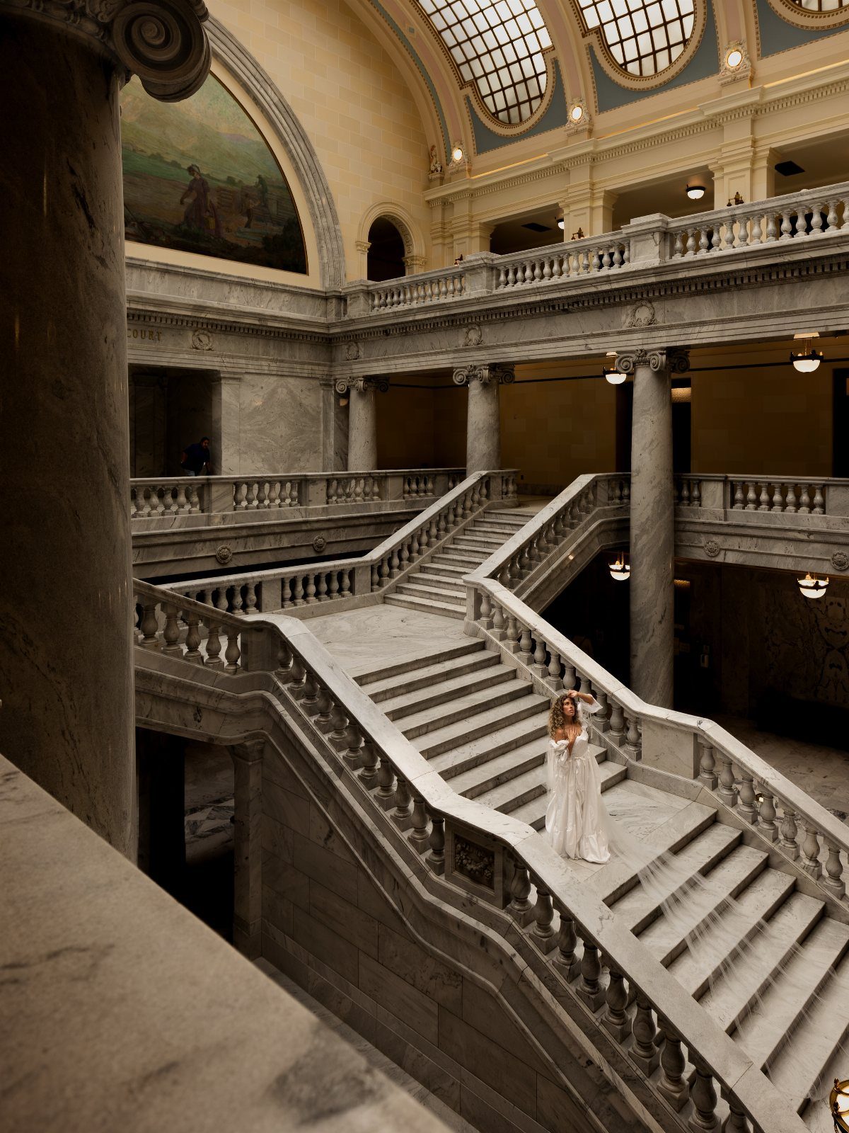 Bride in a white gown posing on a grand marble staircase in a classical hall