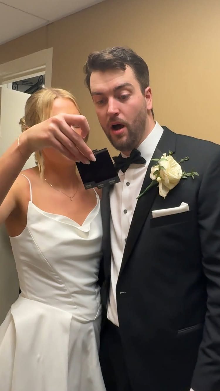 Groom in tuxedo reacting with surprise to a polaroid photo held by bride.