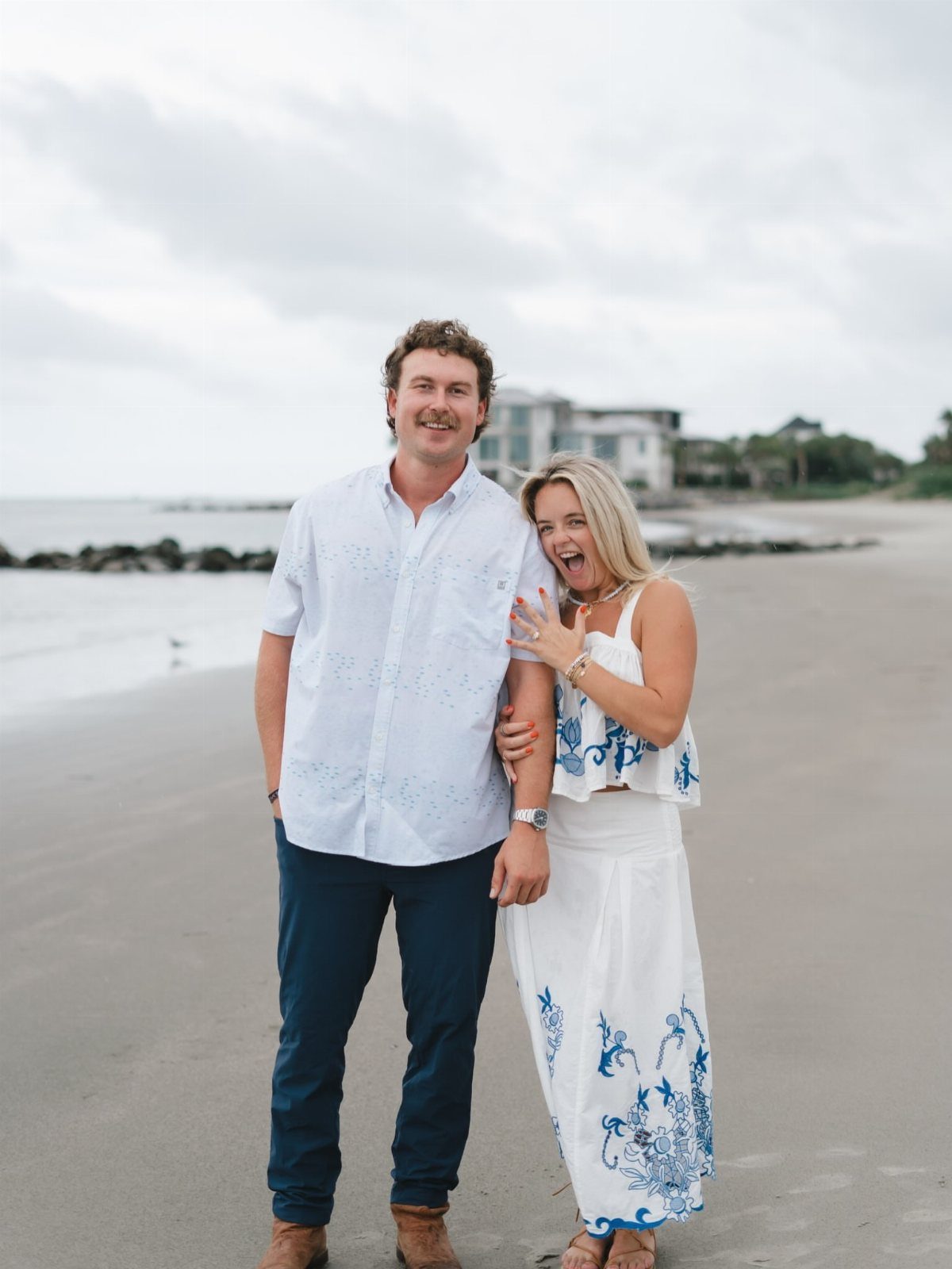Smiling couple posing on a beach wearing white and blue coordinated outfits.