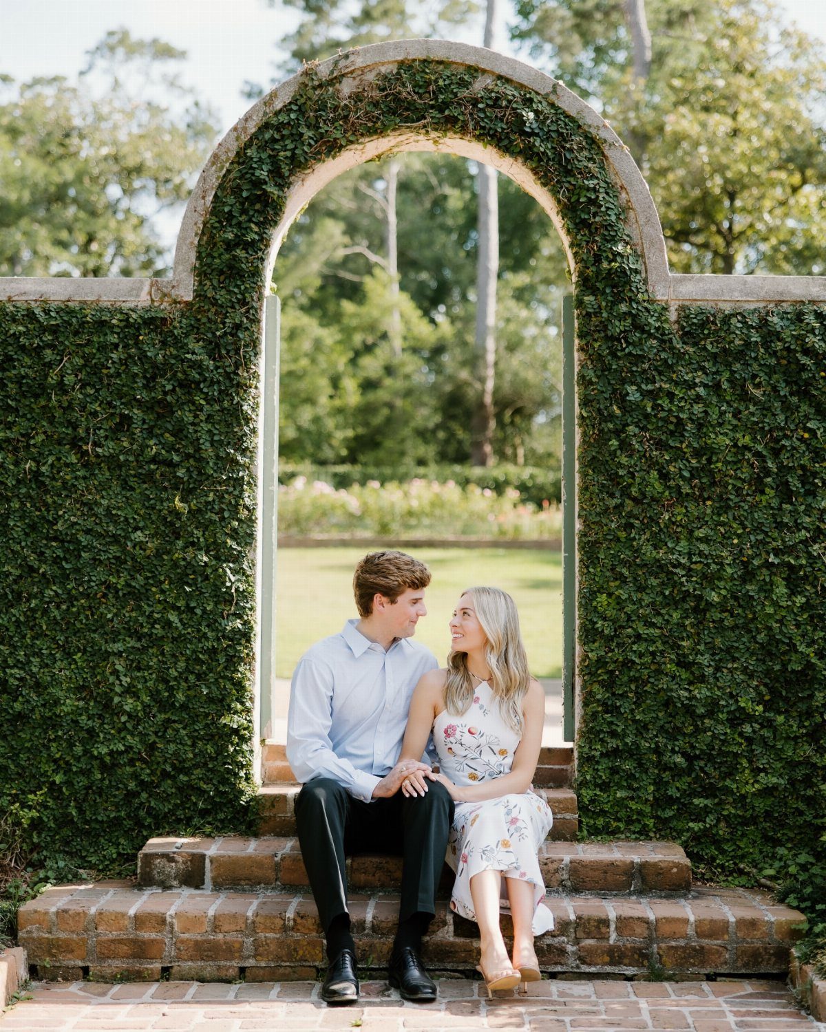 Couple in light blue shirt and floral dress sitting under ivy archway