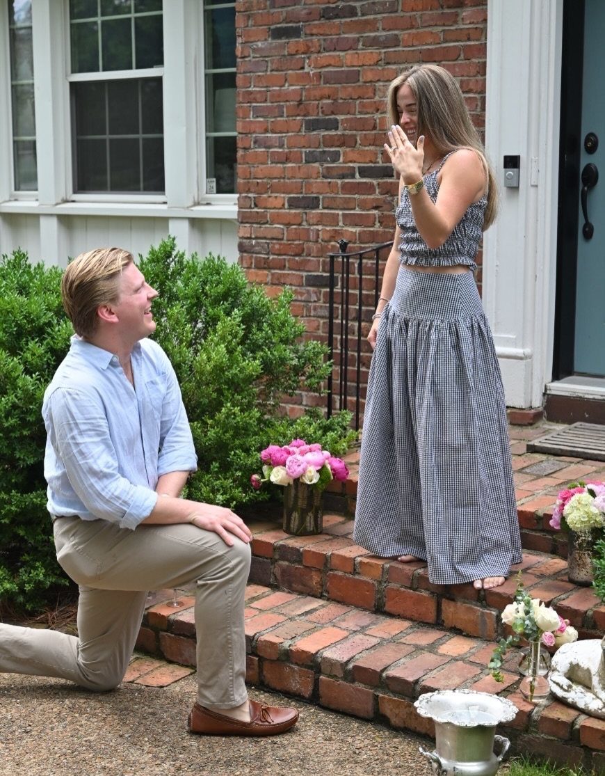 Man proposing to woman on brick steps wearing a gingham two-piece outfit