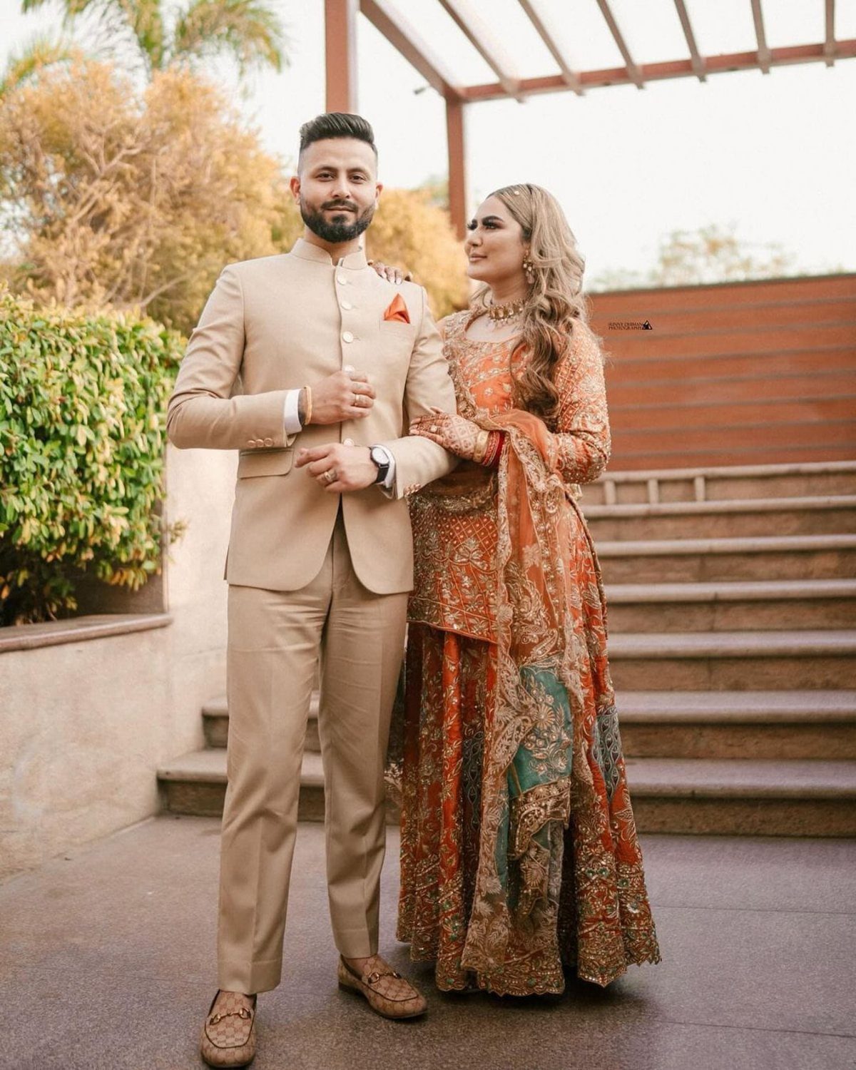 Couple posing in formal attire, woman in an ornate orange embroidered dress.