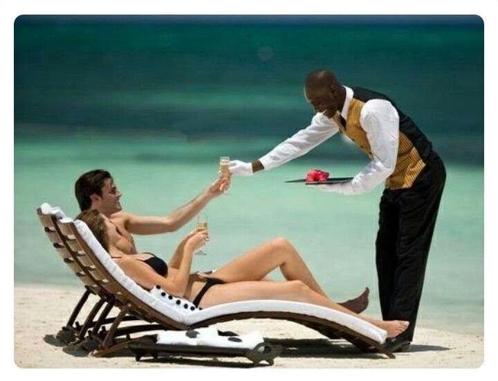 Butler serving drinks to a couple relaxing on beach loungers by the ocean