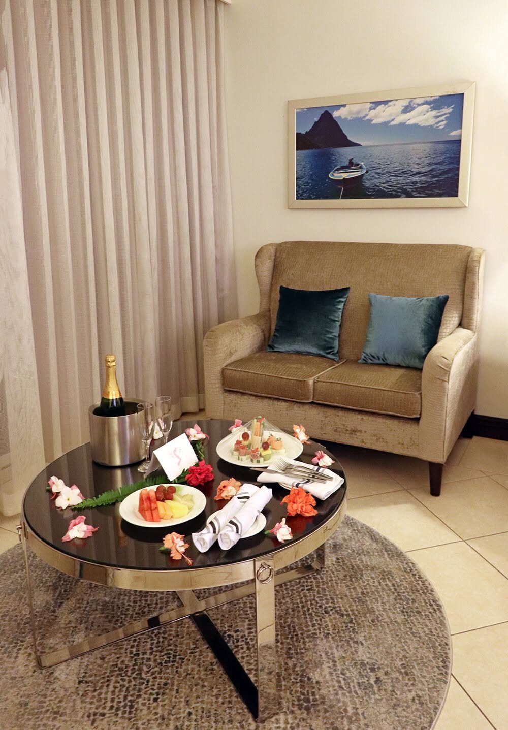 Champagne and fruit platters on a glass table in a resort living room.