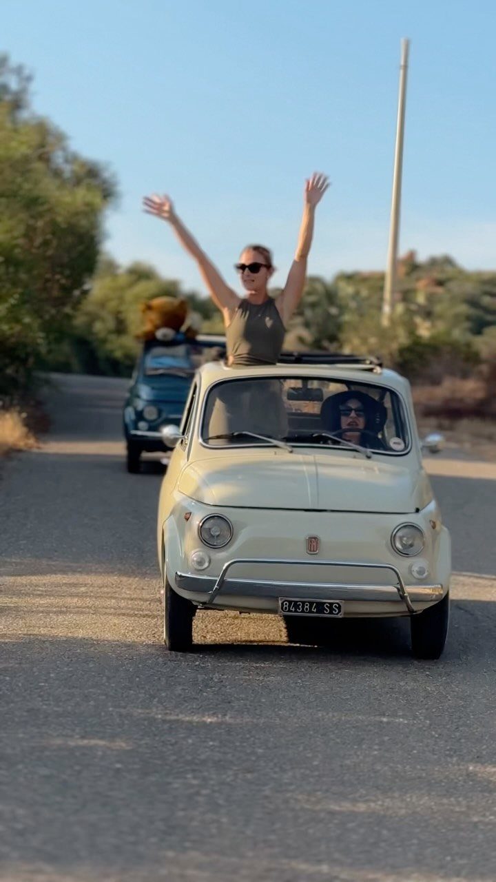 Woman with arms raised in a cream vintage car on a sunny road