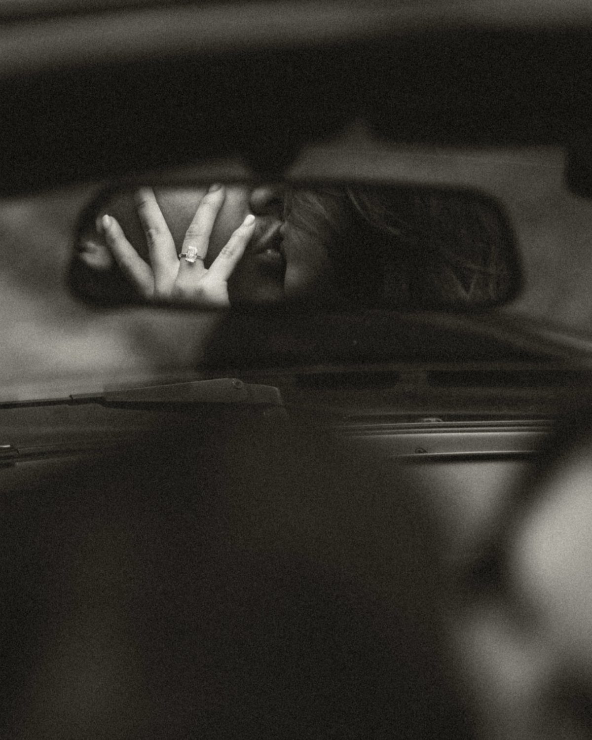 Hand with engagement ring reflected in a car rearview mirror in black and white
