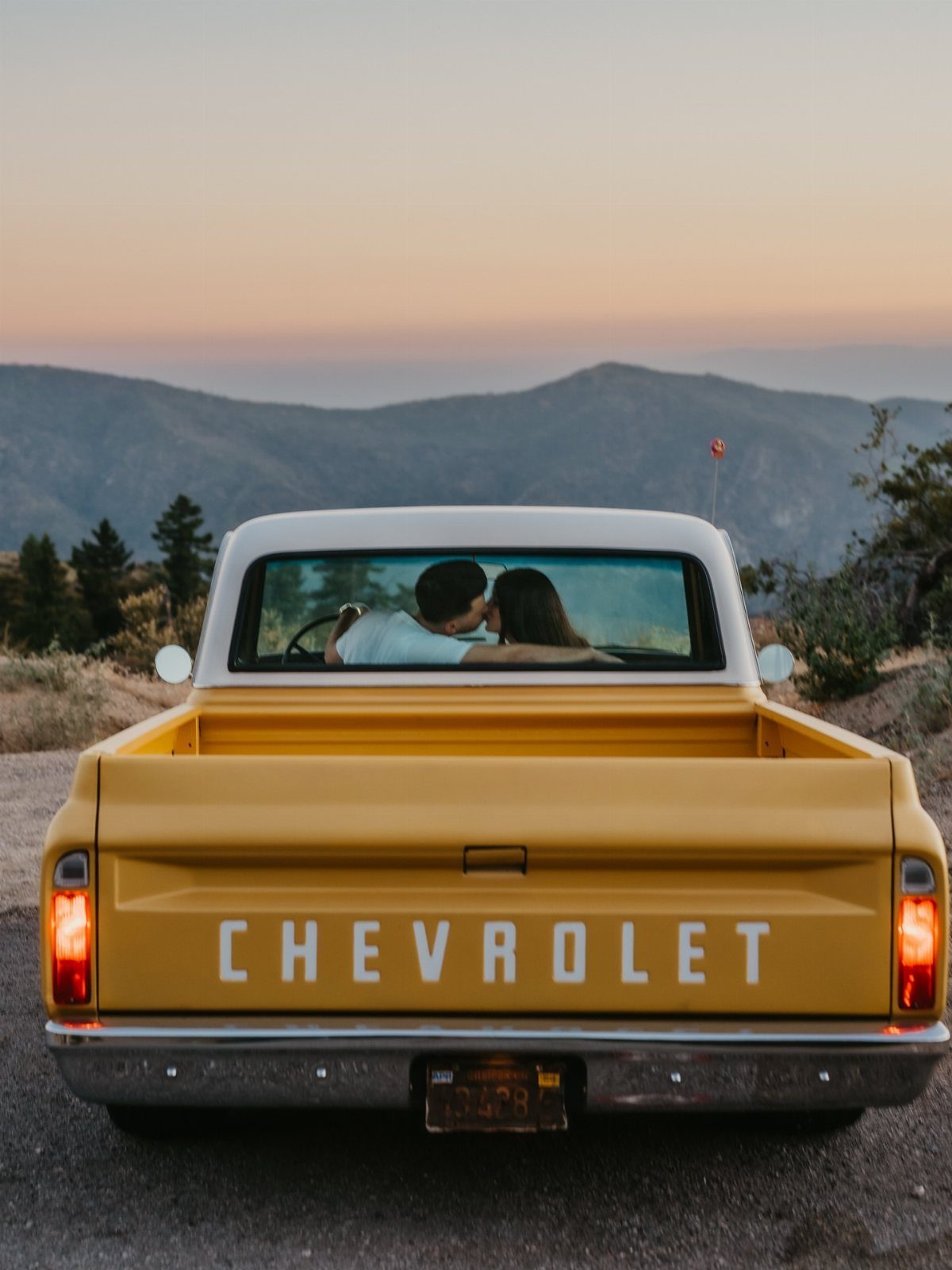 Couple kissing inside a yellow vintage Chevrolet truck overlooking a mountain range