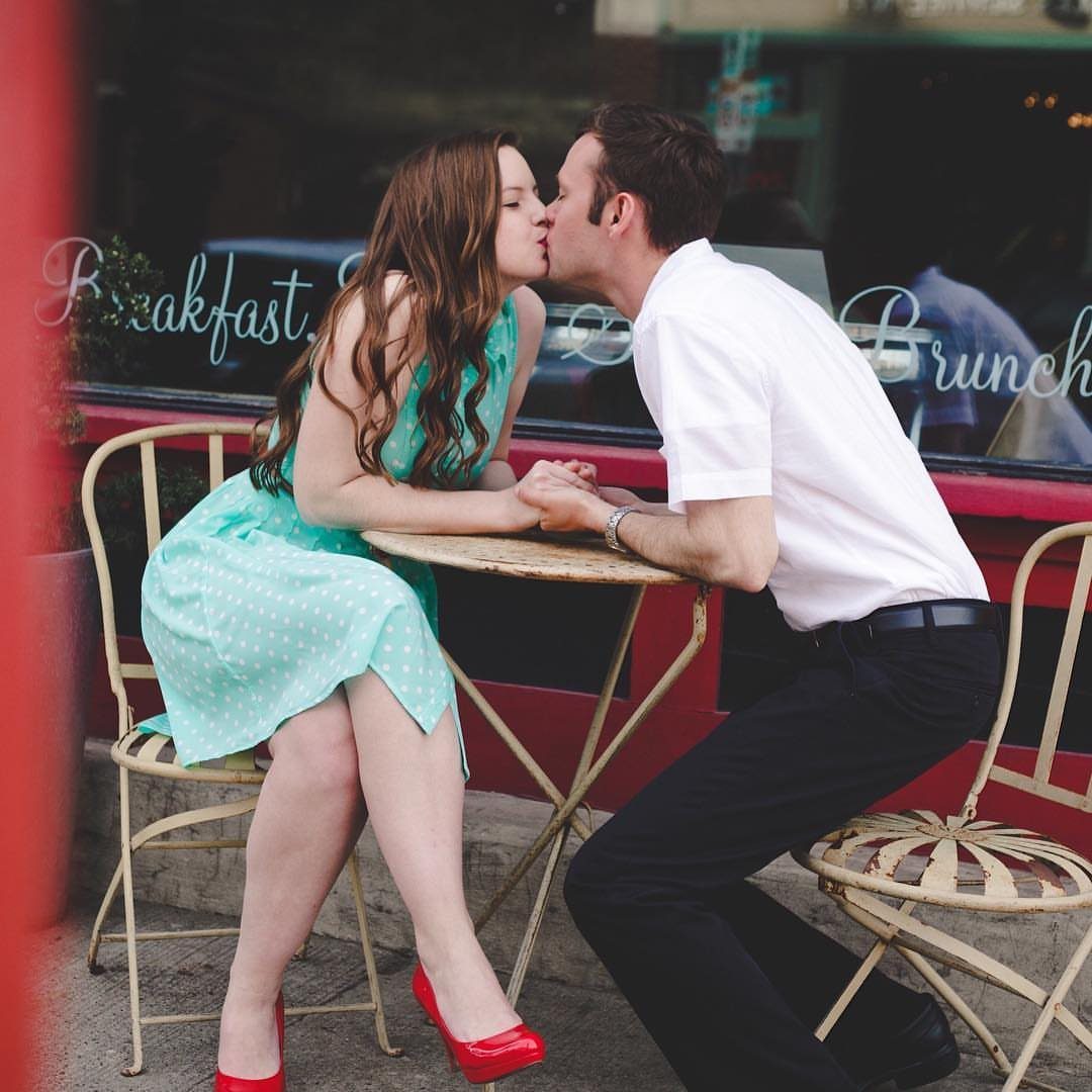 Couple kissing at a cafe table in vintage style clothing and red heels