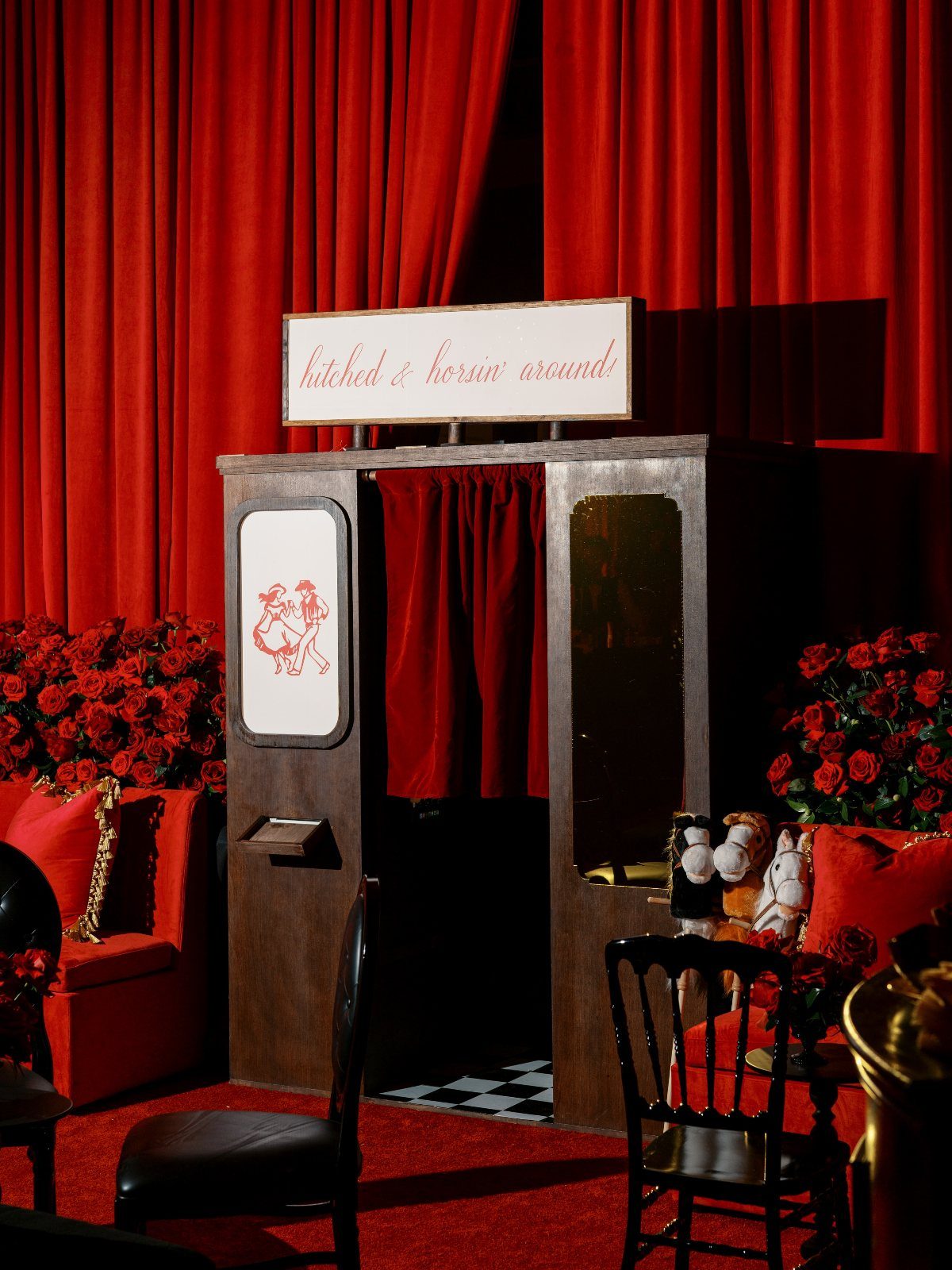 Vintage wooden photo booth with red velvet curtains and floral wedding decorations.