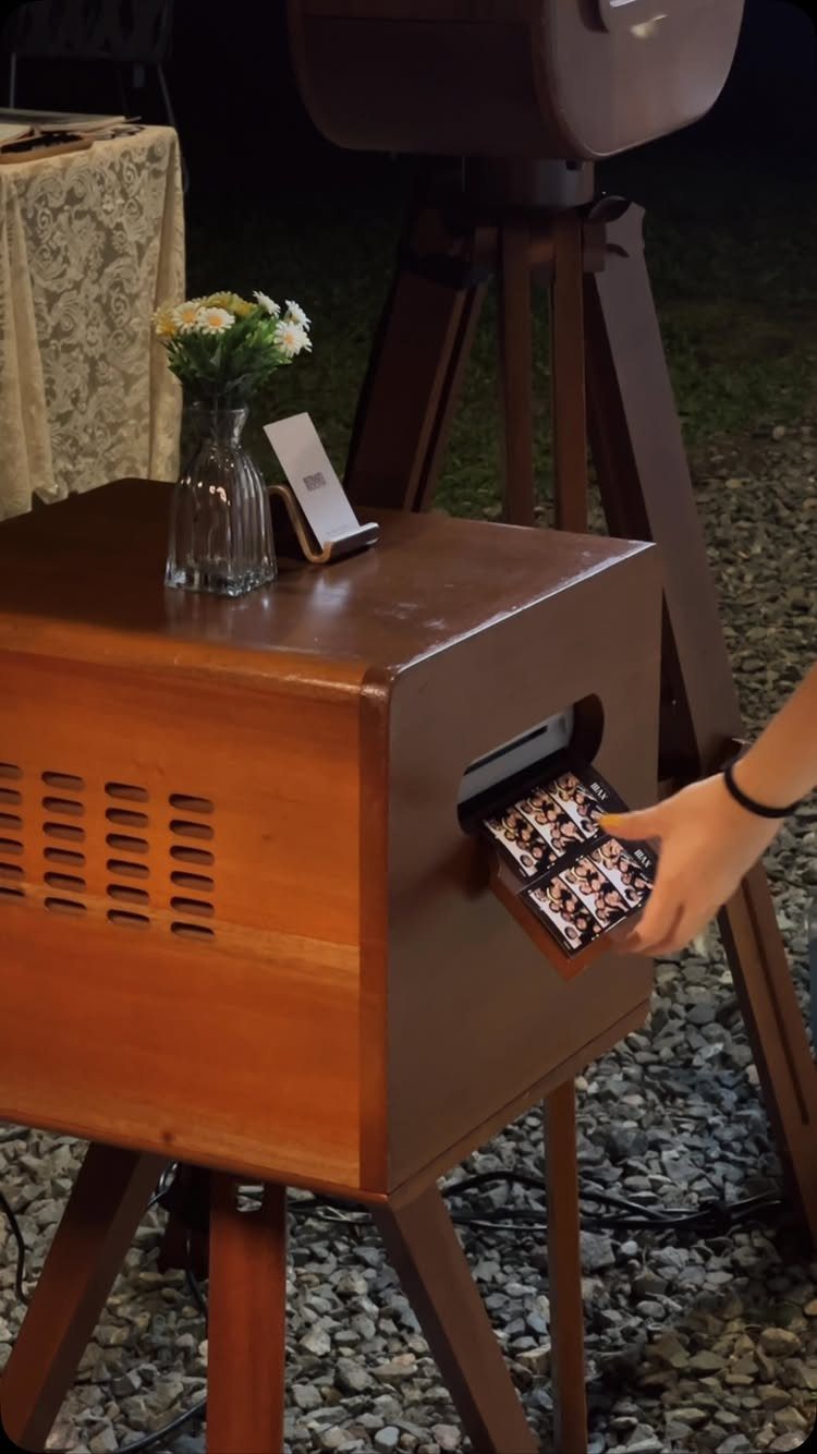 Hand pulling a photo strip from a vintage wooden wedding photo booth box